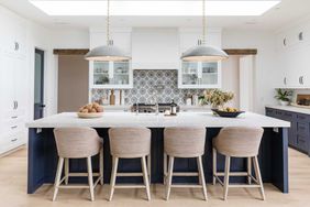 White kitchen with white and blue cabinets, long island with four chairs, hanging pendant lights, and patterned tile backsplash