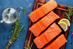 Food background, sliced portions large salmon fillet steaks on chopping board on dark blue concrete table, copy space, top view